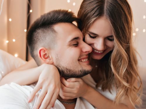 Gorgeous caucasian girl gently embracing boyfriend. Indoor photo of laughing lady with wavy hair spending time with brunette husband.